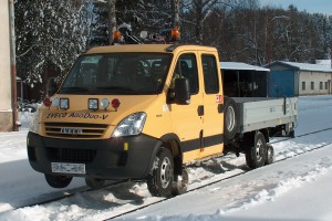 Vehicle can be equipped with platform body with tiltable side plates, container or other superstructures. Constant speed forwards and backwards during ride on rails is achieved by reversible gearbox for constant speed drive forwards and reverse. Electronic display unit is used for monitoring speed, operation and failure conditions.