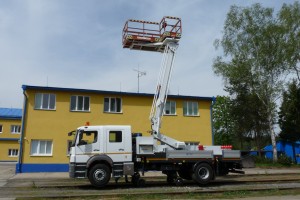 Pracovný koš ramenovej plošiny je v tvare písmena “L“ a vďaka tomuto riešeniu sa obsluha dostane z jednoho miesta aj tzv. za stožiar.